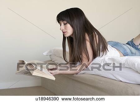 Stock Image - Woman reading book on bed. Fotosearch