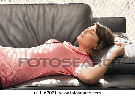 Stock Image - Woman relaxing on a sofa with headphones. Fotosearch