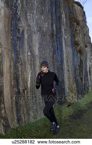 Stock Image - woman running beside rockface. Fotosearch