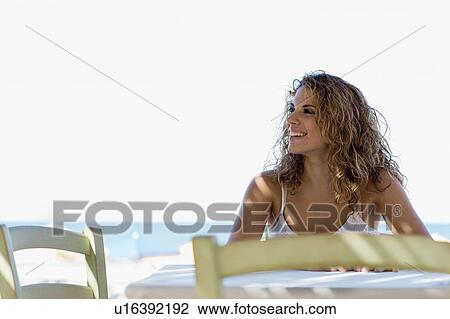 Stock Image - woman sitting at the table at the beach. Fotosearch