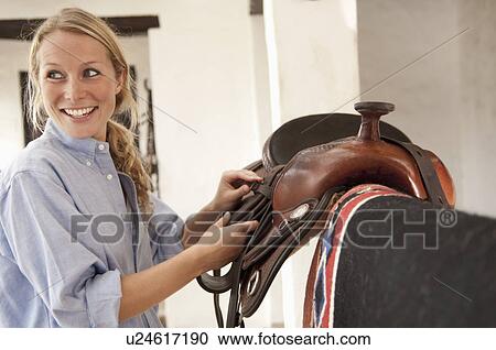 Woman smiling picking up saddle View Large Photo Image Stock Image - Woman smiling picking up saddle. Fotosearch