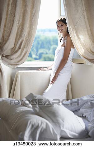 Stock Image - Woman standing by the window in towel. Fotosearch