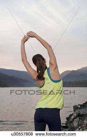 Stock Photo - woman standing in front of lake with water bottle. Fotosearch