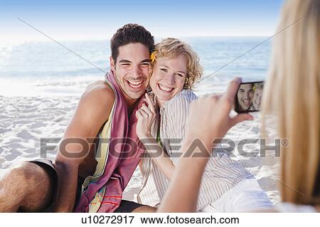 Stock Photo - Woman taking picture of friends on beach. Fotosearch