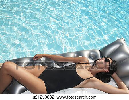 Stock Image - Woman tanning on air bed by the pool. Fotosearch