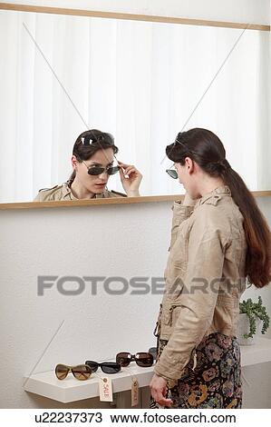 Stock Image - woman trying on sunglasses in mirror. Fotosearch
