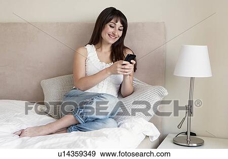 Woman using cell phone on bed View Large Photo Image Stock Photo - Woman using cell phone on bed. Fotosearch