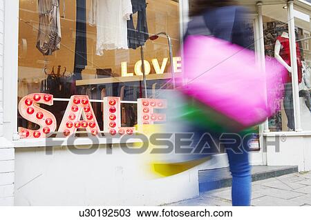 Stock Image - Woman walking past shop. Fotosearch