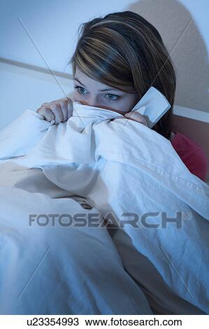 Stock Image - Woman watching tv in bed, frightened. Fotosearch