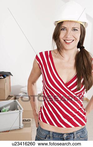 Stock Image - Woman wearing hard hat in new home. Fotosearch