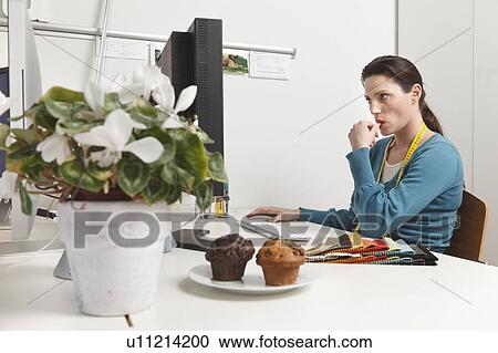Stock Image - Woman working at computer, sucking her thumb. Fotosearch