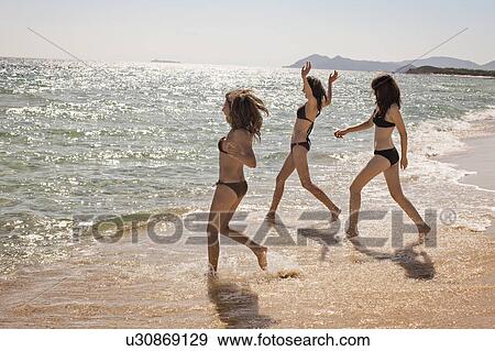 Stock Photo - Women in bikinis playing in surf. Fotosearch