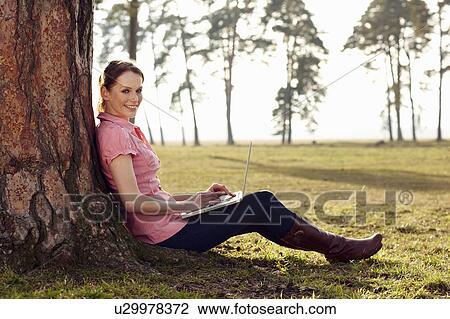 Women leaning on tree with laptop View Large Photo Image Stock Image - Women leaning on tree with laptop. Fotosearch