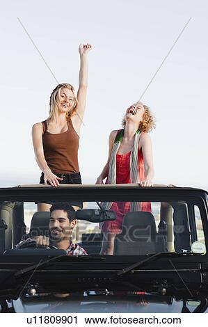 Stock Image - Women standing in jeep on road trip. Fotosearch