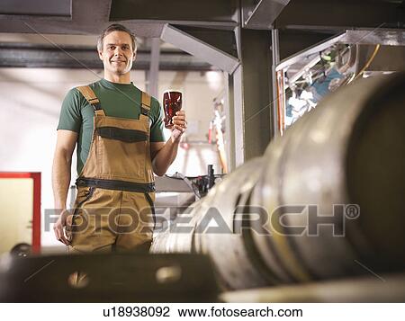Stock Image - Worker holding pint of beer in brewery. Fotosearch