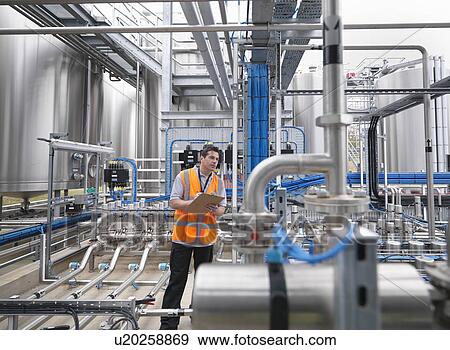 Stock Photo - Worker with machinery in bottling plant. Fotosearch