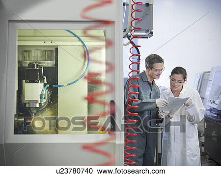 Stock Image - Workers next to computerised lathe. Fotosearch