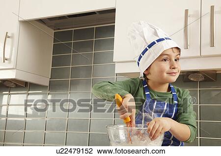 Stock Image - Young boy with mixing bowl in kitchen. Fotosearch