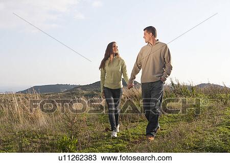 Stock Image - Young couple holding hands and walking. Fotosearch