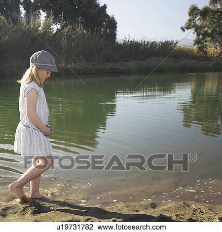 Stock Image - Young girl by river with feet in water. Fotosearch