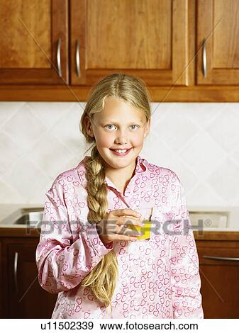 Stock Photo - Young girl holding orange juice in kitchen smiling.. Fotosearch