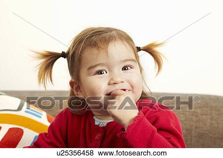 Stock Photo - Young girl on sofa with fingers in mouth. Fotosearch