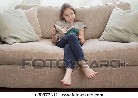 Stock Image - young girl reading book on sofa. Fotosearch