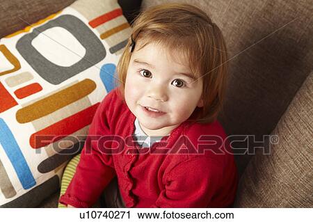 Stock Image - Young girl sitting on sofa looking up. Fotosearch