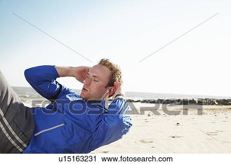Stock Image - Young man doing sit ups on sandy beach. Fotosearch