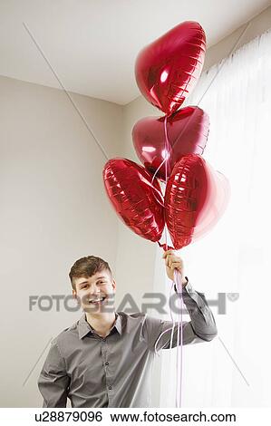 Young man holding heart shaped balloons View Large Photo Image Stock Photograph - Young man holding heart shaped balloons. Fotosearch