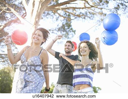 Stock Image - Young man & women running with balloons. Fotosearch