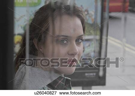 Stock Photo - Young woman at bus shelter in rain. Fotosearch
