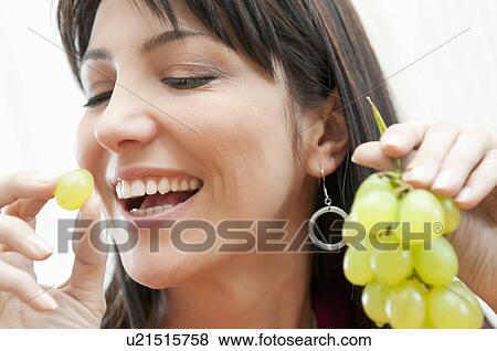 Stock Photo - Young woman eating bunch of grapes. Fotosearch