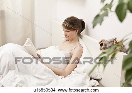 Picture - Young woman in bed, reading. Fotosearch