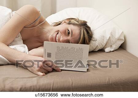 Stock Photograph - Young woman reding in bed. Fotosearch