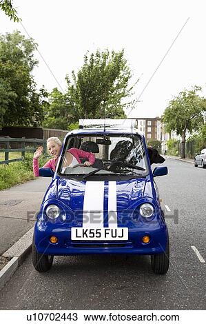 Stock Image - Young woman waving from electric car. Fotosearch