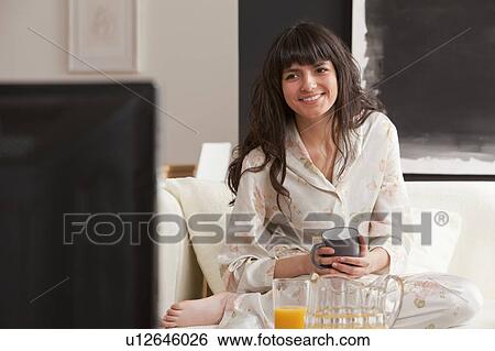 Stock Photograph - Young woman with mug in front of tv. Fotosearch