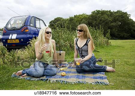 Stock Photograph - Young women pick-nicking by electric car. Fotosearch