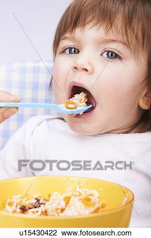 Stock Image - Baby girl being spoon-fed in high chair. Fotosearch