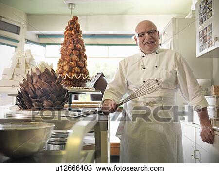 Stock Image - Baker holding whisk in cake shop. Fotosearch