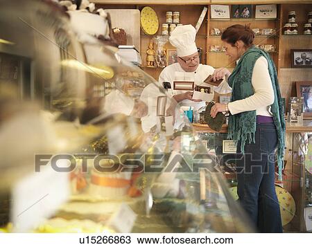 Stock Image - Baker with customer in cake shop. Fotosearch