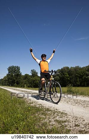 Stock Image - Biker cheering on dirt road. Fotosearch