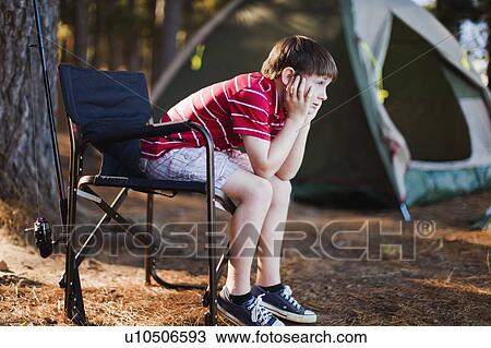 Stock Image - Bored boy in lawn chair at campsite. Fotosearch