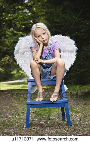 Stock Image - Bored girl in wings sitting on stool. Fotosearch