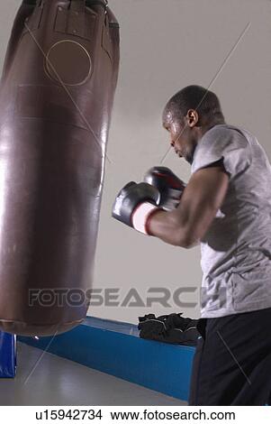 Picture - Boxer using punching bag in gym. Fotosearch