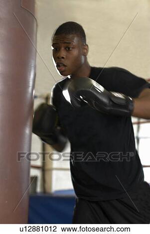 Stock Image - Boxer using punching bag in gym. Fotosearch