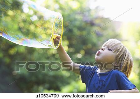 Boy blowing oversized bubble in backyard View Large Photo Image Stock Photo - Boy blowing oversized bubble in backyard. Fotosearch