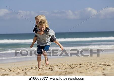 Boy carrying brother piggyback on beach View Large Photo Image Stock Photo - Boy carrying brother piggyback on beach. Fotosearch