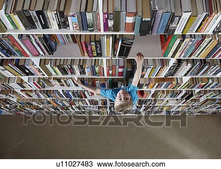 Stock Image - Boy climbing bookshelves. Fotosearch