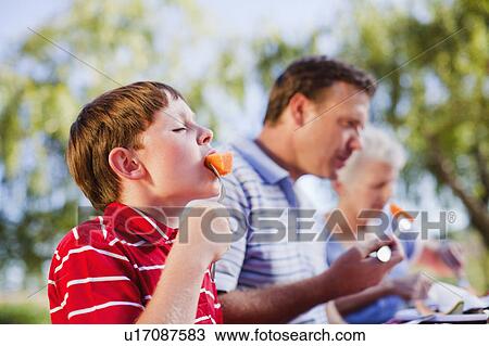 Boy eating melon at picnic table View Large Photo Image Stock Image - Boy eating melon at picnic table. Fotosearch